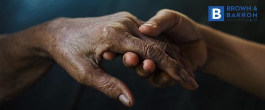 A younger hand holds the hand of an elderly person