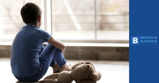 Sad little boy sitting on floor beside window