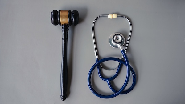 A judges gavel and a blue stethoscope are placed side by side on a gray background, symbolizing the intersection of law and medicine.